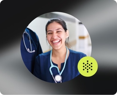 A smiling clinician in scrubs, lit in a circle against a dark studio background.