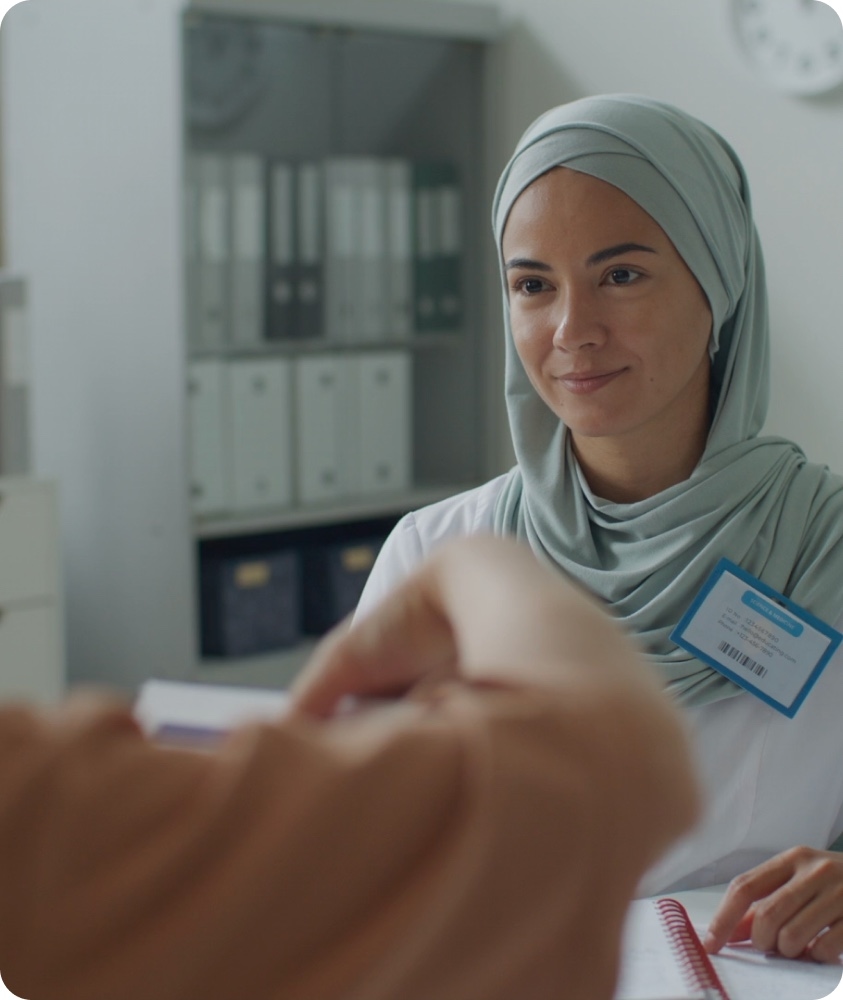 A clinician in a headscarf smiling as she sits with a patient.