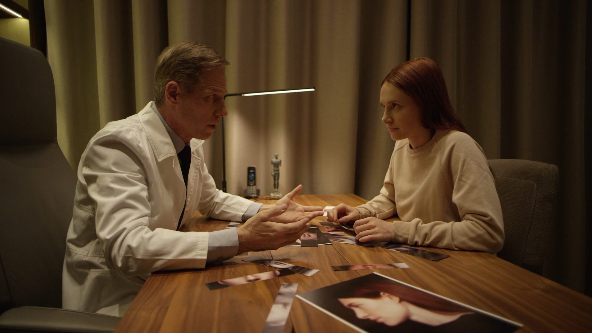 A surgeon talking a patient through before-and-after photographs across a consulting-room table.